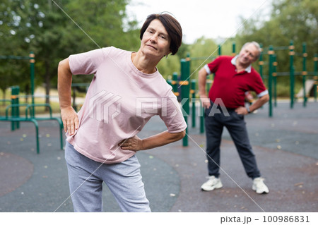 Aged man and woman practicing gymnastics in open-air sports area Aged man and woman practicing gymnastics in open-air sports area 100986831