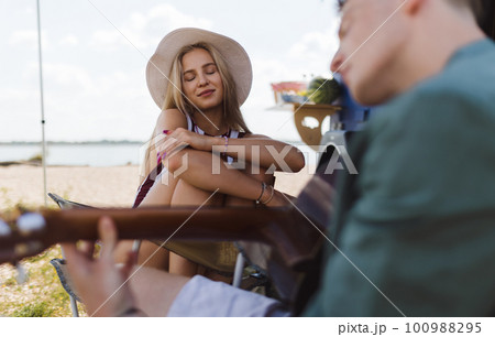Young couple sitting together in front of van, camping and playing at guitair. 100988295