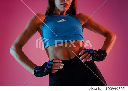 Close up of sporty slim young fitness woman standing, holding hands on waist on studio background 100990705