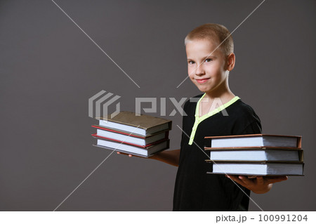 Cute boy holding stacks of books on gray background 100991204