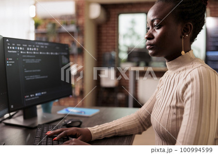 African american programmer typing big data code on computer, sitting at desk developing program using html script. Tech enginner writing ai algorithm working in it programming agency 100994599