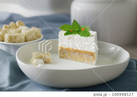 White mousse cake decorated with mint leaf on plate on grey table cloth 100998527