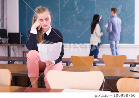 Frustrated girl student sitting in classroom with paper 100998760