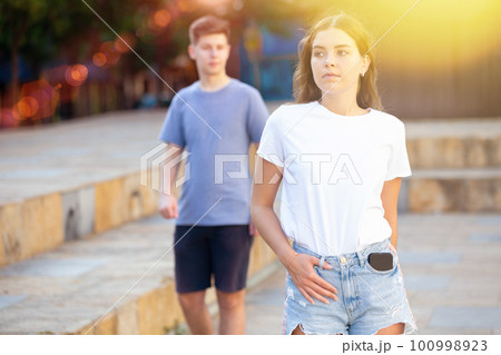 Cute teen girl in denim shorts walking down street 100998923