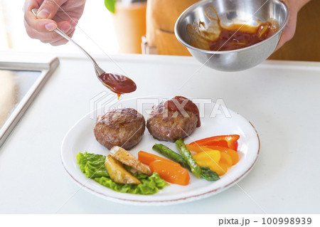 盛り付けたハンバーグにソースをかける 100998939