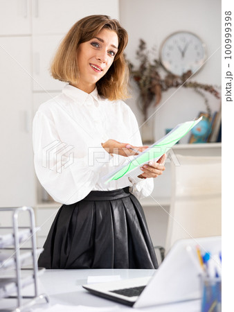 Positive girl secretary with folder for documents in office Positive girl secretary with folder for documents in office 100999398