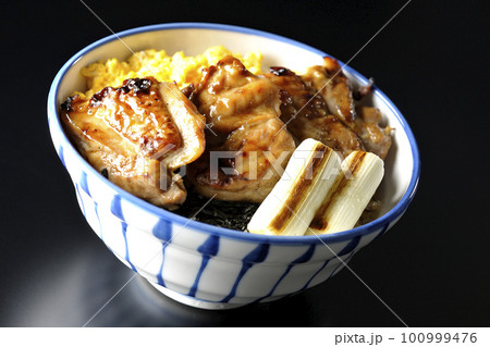 そぼろ玉子と焼き葱と刻み海苔も一緒に乗ってる照り焼きチキン丼を黒背景で撮影 100999476