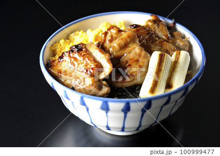 そぼろ玉子と焼き葱と刻み海苔も一緒に乗ってる照り焼きチキン丼を黒背景で撮影 100999477