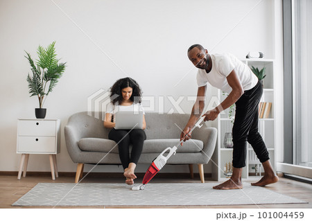 Husband cleaning with vacuum while wife working on laptop Husband cleaning with vacuum while wife working on laptop 101004459