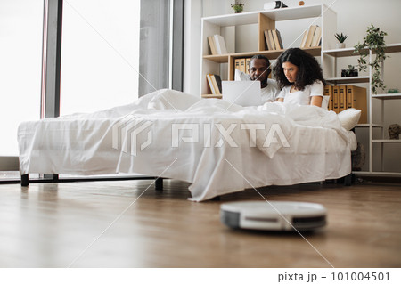 Multiracial family of two using laptop and robot vacuum 101004501