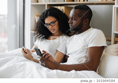 Multiracial family reading article on smartphones in bed 101004584