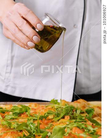 Chef pouring olive oil on pizza 101006927