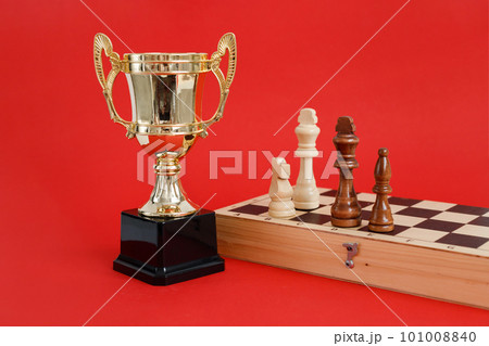 Winner golden cup and Chess board with wooden figures still life on red background Winner golden cup and Chess board with wooden figures still life on red background 101008840