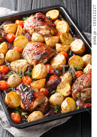 Balsamic chicken with potatoes, red onion and tomatoes close-up on a baking sheet. Vertical 101012227