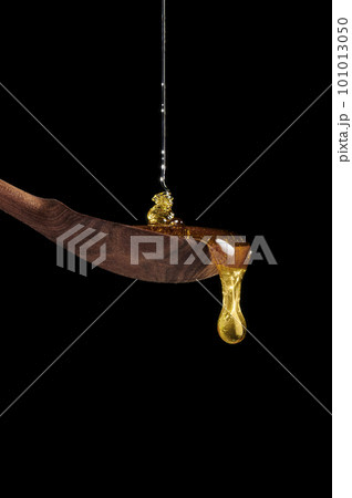 Honey pouring on wooden spoon and dripping from spoon. Dark background. A drop of honey glows in the sun. 101013050