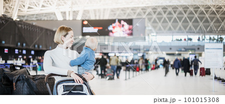 Motherat travelling with his infant baby boy child, walking, pushing baby stroller and luggage cart at airport terminal station. Travel with child concept Motherat travelling with his infant baby boy child, walking, pushing baby stroller and luggage cart at airport terminal station. Travel with child concept 101015308