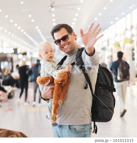 Father traveling with child, holding his infant baby boy at airport terminal waiting to board a plane waving goodby. Travel with kids concept 101015315