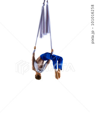 Dynamic image of young man, professional, flexible aerial gymnast doing acrobatic tricks with aerial ribbon against white studio background 101016258