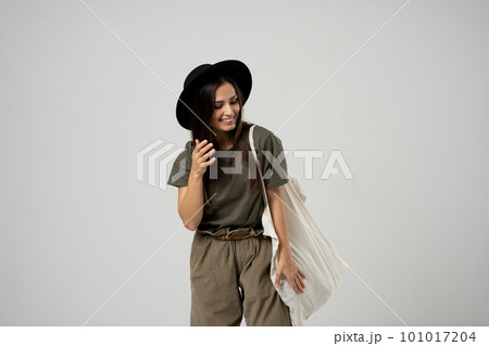 Brunette woman in green t-shirt and black hat holding cotton shopper bag with vegetables, products in white room. Eco friendly shopping bags. Zero waste, plastic free concept. Brunette woman in green t-shirt and black hat holding cotton shopper bag with vegetables, products in white room. Eco friendly shopping bags. Zero waste, plastic free concept. 101017204