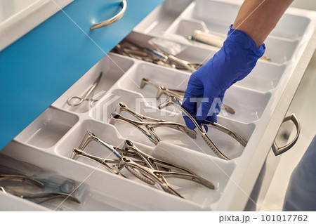 Doctor's hands wearing a disposable medical gloves holding a stainless steel nasal speculum for ENT examination over other surgery instruments Doctor's hands wearing a disposable medical gloves holding a stainless steel nasal speculum for ENT examination over other surgery instruments 101017762