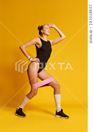 Portrait of sporty girl wearing swimsuit and doing exercise with rubber bands for sport over yellow background Portrait of sporty girl wearing swimsuit and doing exercise with rubber bands for sport over yellow background 101018637