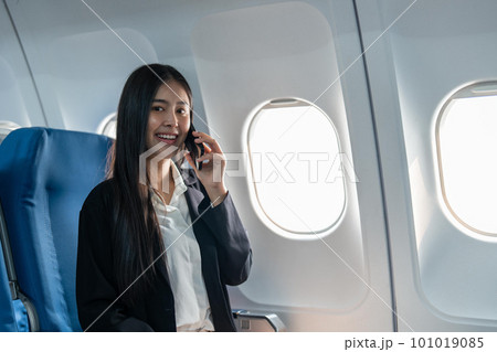 Successful young business woman working speaking on mobile phone while while sitting on aircraft cabinin 101019085
