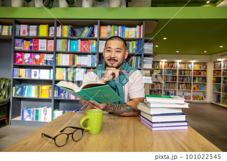 Young asian man sitting with a book in library Young asian man sitting with a book in library 101022545