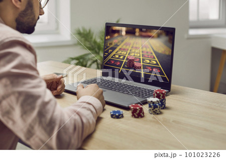 Young man sitting at the desk and playing gambling in online casino at home. 101023226