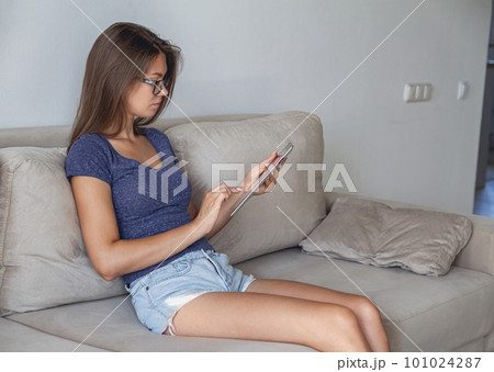 Young woman sitting on sofa and using tablet at home Young woman sitting on sofa and using tablet at home 101024287