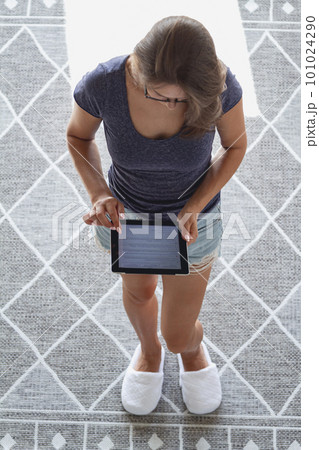 Young woman stands on the carpet in living room and holds a tabl 101024290