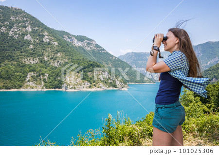 Young woman using binoculars exploring the nature at the Piva lake in Montenegro Young woman using binoculars exploring the nature at the Piva lake in Montenegro 101025306