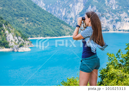 Young woman using binoculars exploring the nature at the Piva lake in Montenegro Young woman using binoculars exploring the nature at the Piva lake in Montenegro 101025313