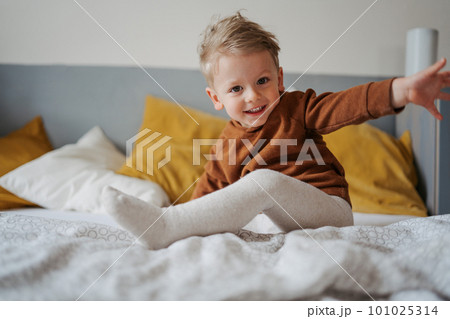 Portrait of little boy sitting on a bed. 101025314