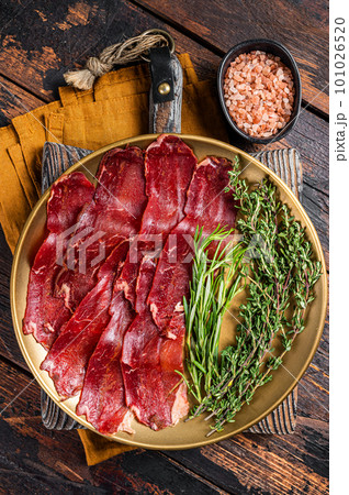 Basturma, sliced dried beef meat, meat Jerky in steel plate with herbs and spices. Wooden background. Top view 101026520
