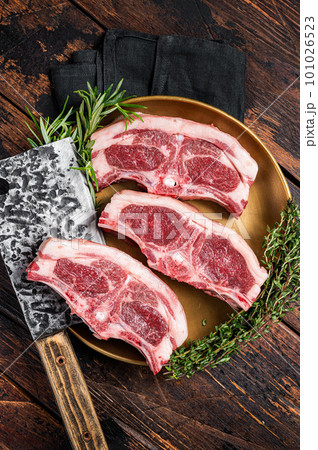 Uncooked Raw lamb loin chops steaks, saddle in plate with rosemary and thyme. Wooden background. Top view 101026523