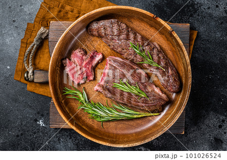 Fried sirloin flap or flank beef steak with herbs in a wooden plate. Black background. Top view 101026524