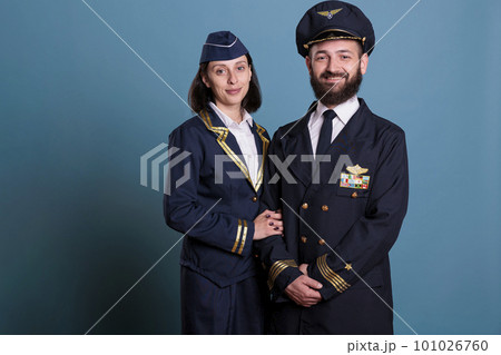 Smiling airplane captain and flight attendant in professional cabin uniform studio, medium shot portrait, aircrew looking at camera. Plane pilot and stewardess, professional team Smiling airplane captain and flight attendant in professional cabin uniform studio, medium shot portrait, aircrew looking at camera. Plane pilot and stewardess, professional team 101026760