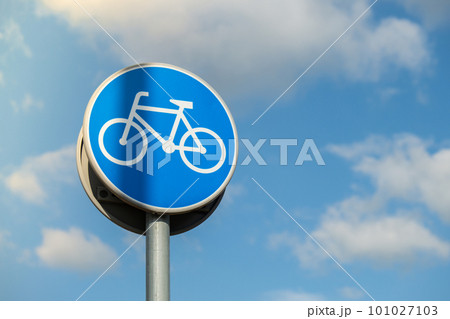 Round road sign depicting white bicycle on blue background, meaning mandatory bike path for cyclists against blue sky background. Blue round sign on bike path pole 101027103