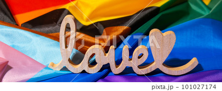 Banner Wooden word love with heart romance on Rainbow LGBTQIA flag made from silk material. Valentine's Day greeting card. Symbol of LGBTQ pride month. Equal rights. Peace and freedom. Support LGBTQIA 101027174