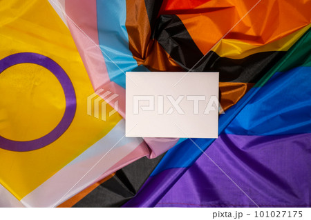 Empty paper blank on Rainbow LGBTQIA flag made from silk material. Mock up template copy space for your text. Symbol of LGBTQ pride month. Equal rights. Peace and freedom. Support LGBTQIA community 101027175