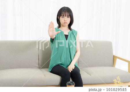 ソファに座ってNGのサインをする若い女性 101029585