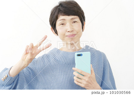 スマホを持ってピースサインする中年女性　白背景 101030566