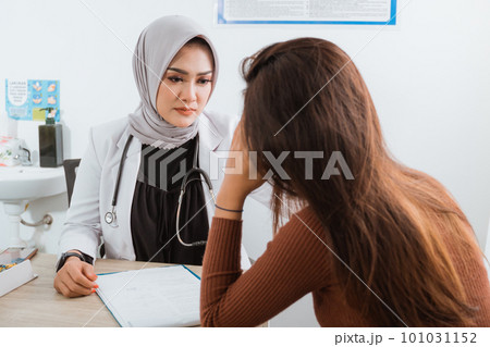 a female doctor look at the female patient that touch her head 101031152