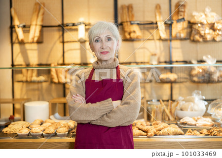 Elderly bakery saleswoman in maroon apron posing with arms crossed Elderly bakery saleswoman in maroon apron posing with arms crossed 101033469