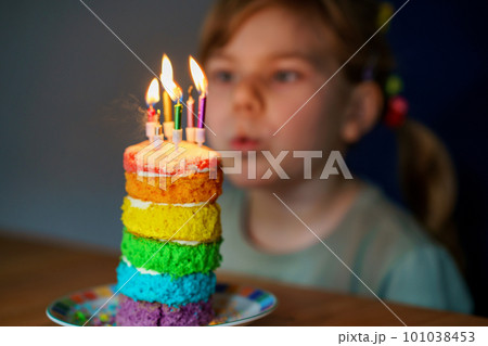 Happy little preschool girl celebrating birthday. Closeup of child with homemade rainbow cake, indoor. Happy healthy toddler blowing six candles on cake. Selective focus on cake Happy little preschool girl celebrating birthday. Closeup of child with homemade rainbow cake, indoor. Happy healthy toddler blowing six candles on cake. Selective focus on cake 101038453