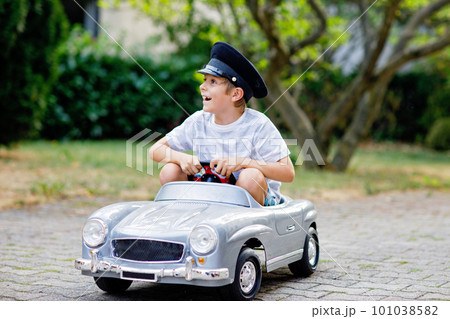 Happy kid boy playing with big old toy car in summer garden, outdoors. Healthy child driving old vintage car taxi. Laughing and smiling kid. Family, childhood, lifestyle concept Happy kid boy playing with big old toy car in summer garden, outdoors. Healthy child driving old vintage car taxi. Laughing and smiling kid. Family, childhood, lifestyle concept 101038582