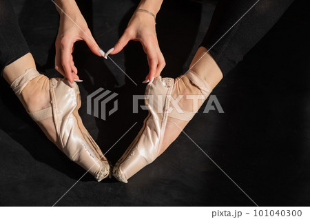 A faceless ballerina sits on the floor and makes a heart shape with her hands and pointe shoes. Top view. A faceless ballerina sits on the floor and makes a heart shape with her hands and pointe shoes. Top view. 101040300