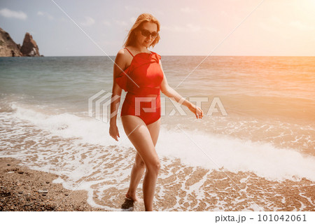 Young woman in red bikini on Beach. Blonde in sunglasses on pebble beach enjoying sun. Happy lady in one piece red swimsuit relaxing and sunbathing by turquoise sea ocean on hot summer day. Close up Young woman in red bikini on Beach. Blonde in sunglasses on pebble beach enjoying sun. Happy lady in one piece red swimsuit relaxing and sunbathing by turquoise sea ocean on hot summer day. Close up 101042061