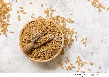Bowl of raw dry rye grain with a wooden spoon on white table top view 101043609