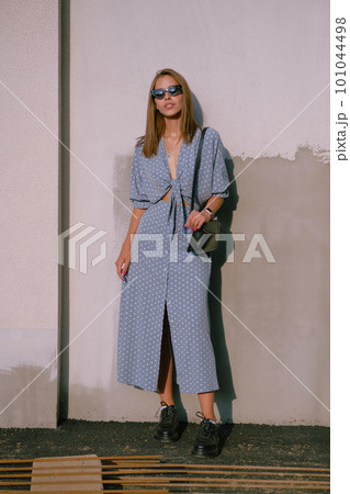 Blonde girl in long blue dress, sunglasses and a small black handbag on her shoulder is walking alone in the city. Fashion and style. Full length. Blonde girl in long blue dress, sunglasses and a small black handbag on her shoulder is walking alone in the city. Fashion and style. Full length. 101044498